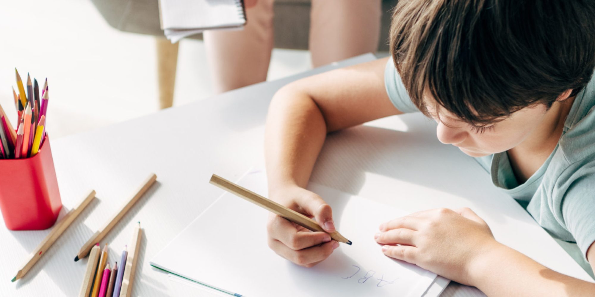 panoramic shot of kid with dyslexia drawing on paper with pencil